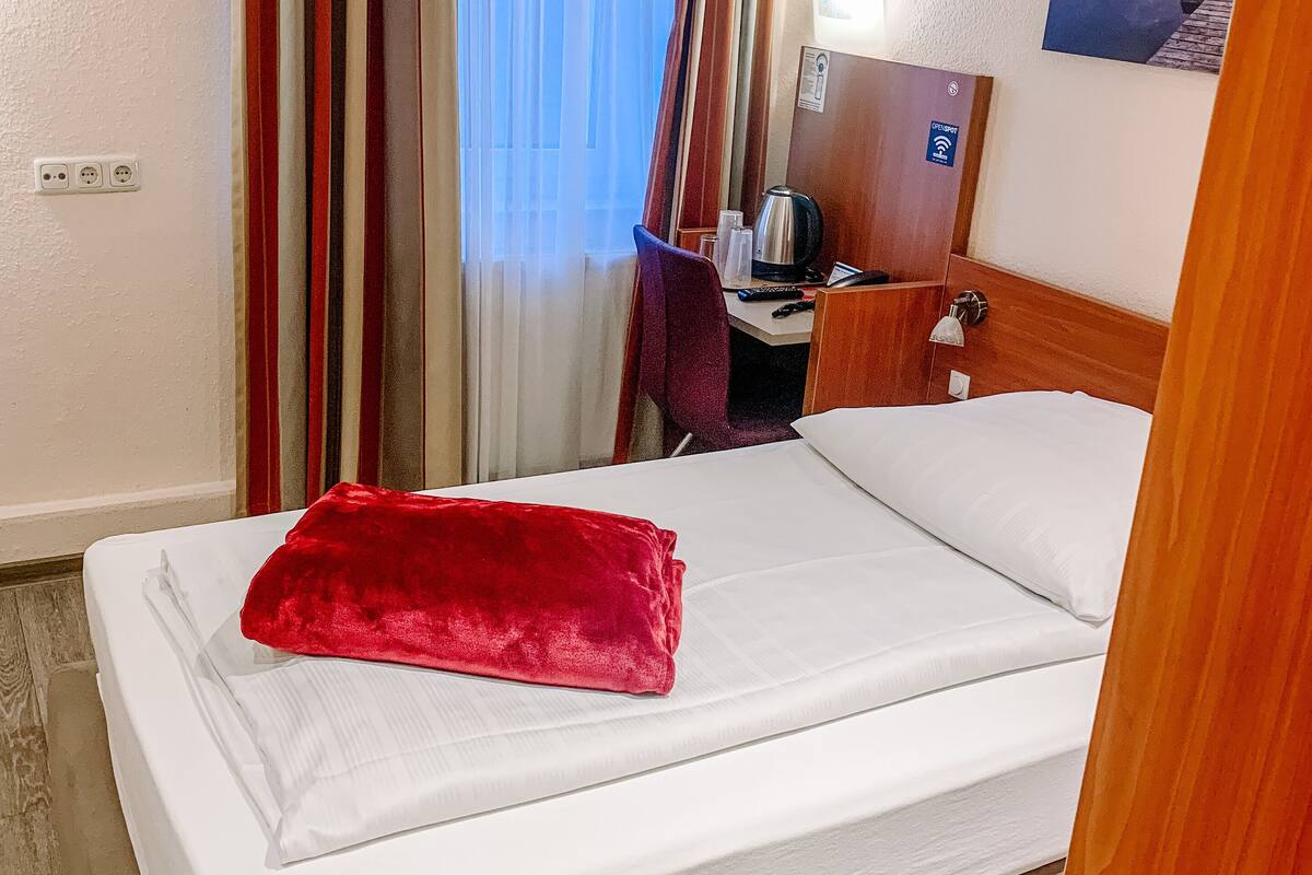 Hotellihuone, jossa on sänky, työpöytä, tuoli, kahvinkeitin ja taulu seinällä.