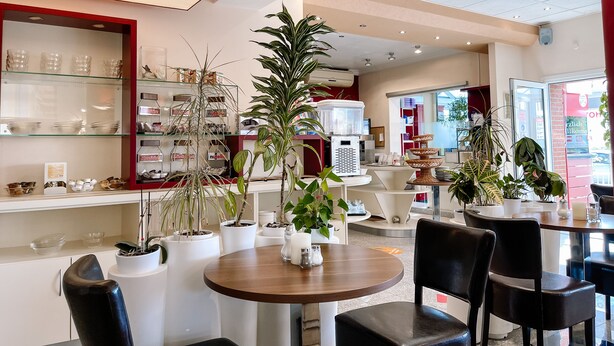 A cafe with round tables, chairs, and potted plants. - Hotel Falk (Bremen)