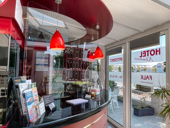 A hotel reception area with a glass counter, red pendant lights, and a view of the hotel entrance.