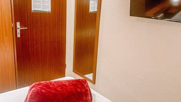 Une chambre d’hôtel avec un lit, un oreiller rouge, des portes en bois et un téléviseur fixé au mur.