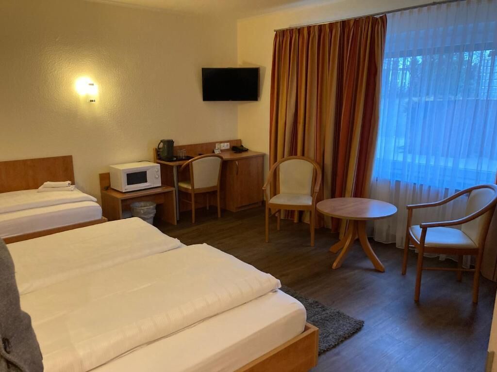 Habitación de hotel con dos camas, un escritorio con computadora, un televisor y una ventana con cortinas.