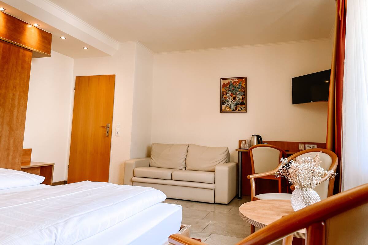 Hotellihuone, jossa on sänky, sohva, tuoli, televisio ja taulu seinällä.