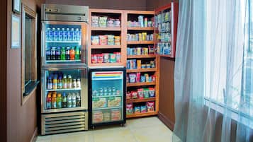 A corner of a room with a vending machine, a refrigerator, and shelves stocked with snacks and beverages.