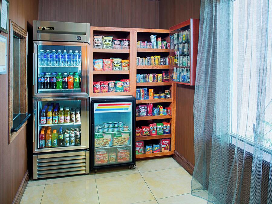 A corner of a room with a vending machine, a refrigerator, and shelves stocked with snacks and beverages.