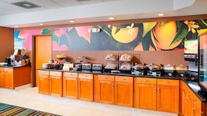 A hotel breakfast area with a buffet setup, wooden cabinets, and a colorful mural on the wall.