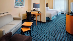 A hotel room with a sofa, desk, chair, two beds, a TV, and a patterned carpet.