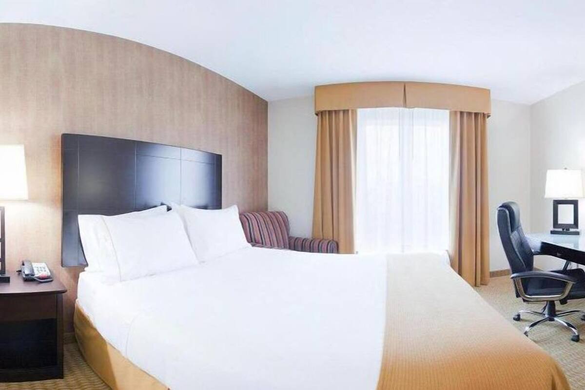 A hotel room with a large bed, a desk with a chair, a lamp, and a window with curtains.