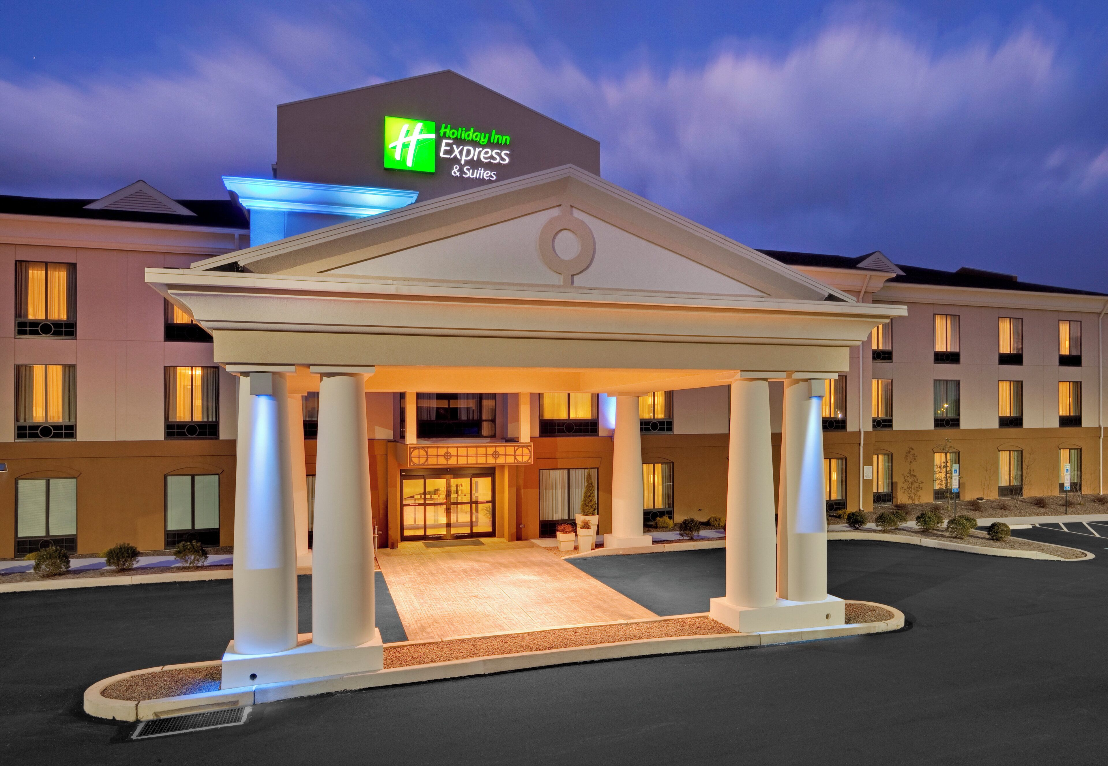 Un Holiday Inn Express & Suites con un padiglione d'ingresso centrale, diversi piani e un'area di parcheggio.