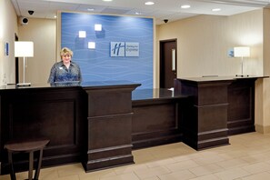 A reception desk area with a blue wall featuring a wave pattern and the Holiday Inn Express logo. There are two receptionists standing behind the desks, and a check-in counter is visible. - Holiday Inn Express Hotel & Suites Lebanon by IHG (Lebanon)