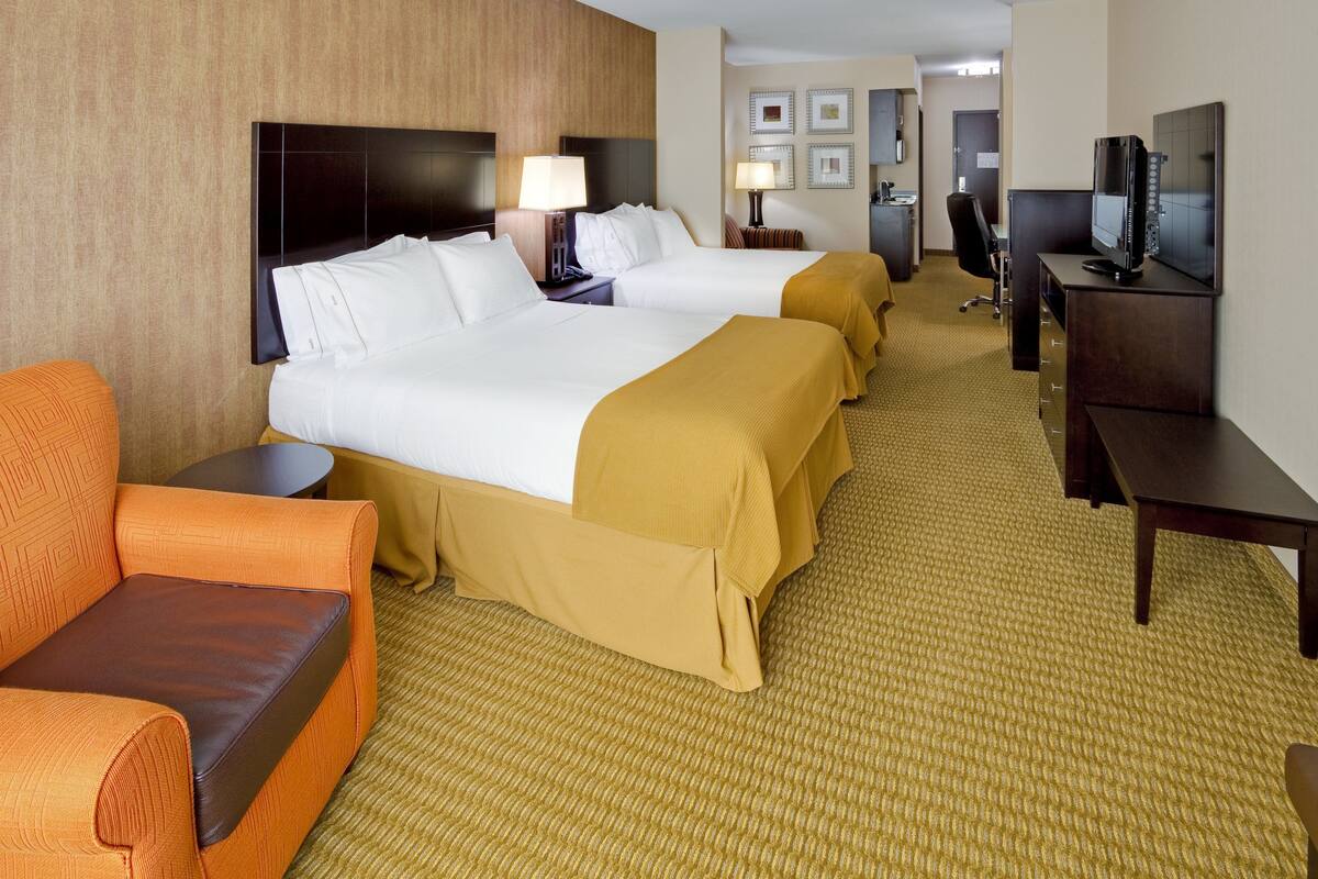 A hotel room with two beds, a sofa, a desk with a TV, and a small table with a lamp.