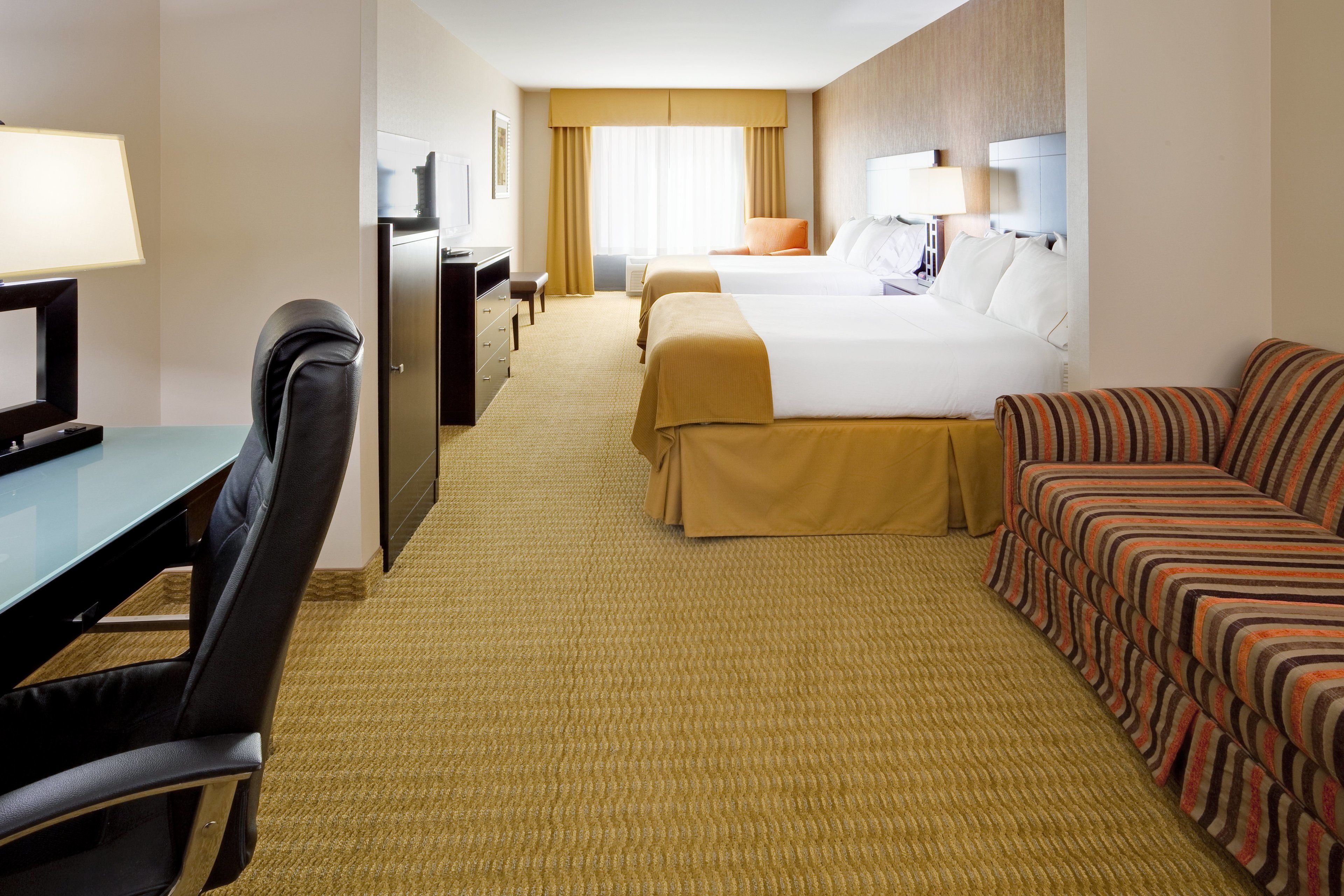A hotel room with a desk, two beds, a sofa, and a television.