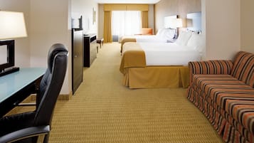 A hotel room with a desk, two beds, a sofa, and a television.