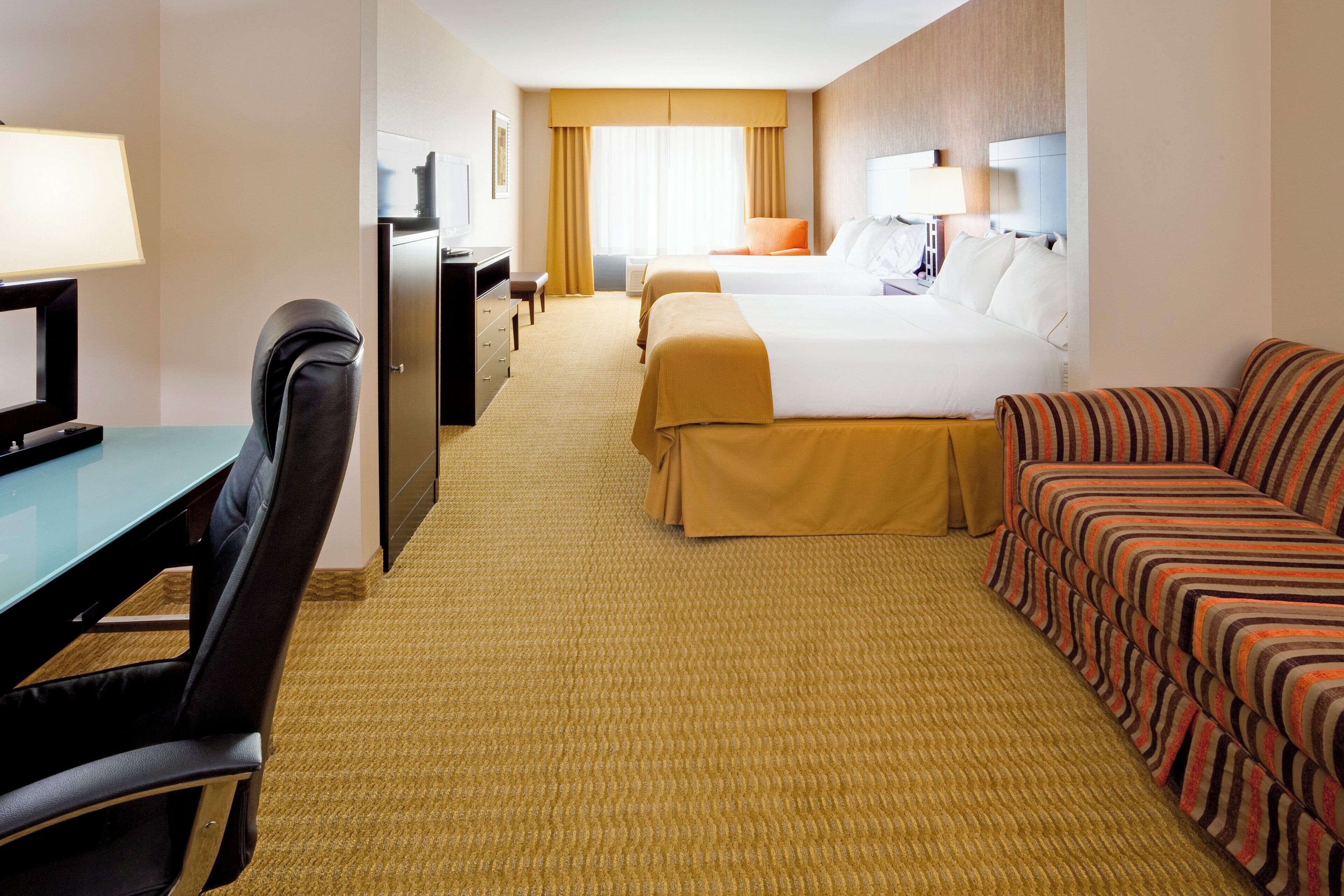 A hotel room with a desk, two beds, a sofa, and a TV.