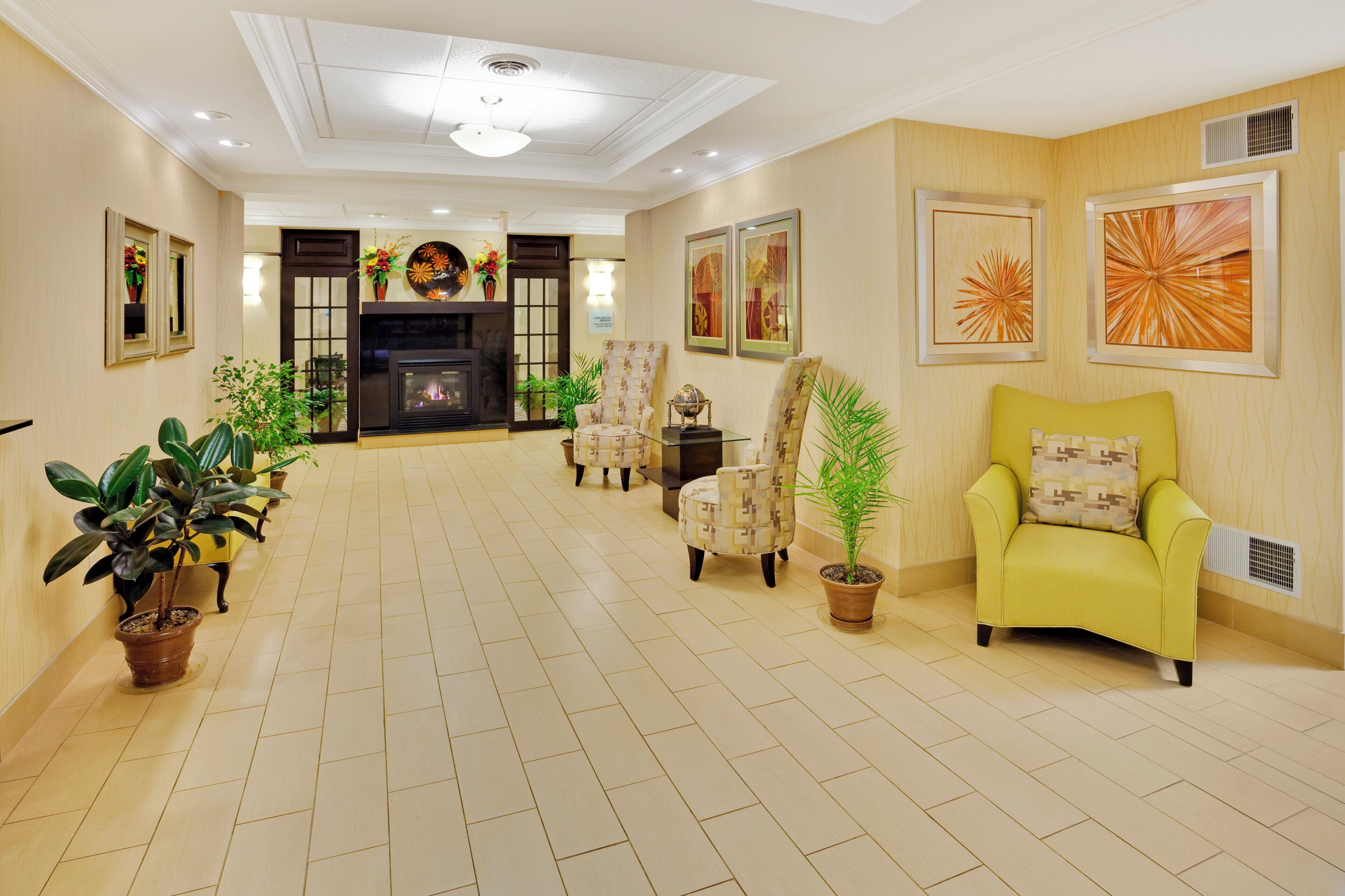 A spacious living room with a fireplace, multiple chairs, potted plants, and artwork on the walls.