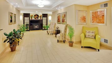 A spacious living room with a fireplace, multiple chairs, potted plants, and artwork on the walls.
