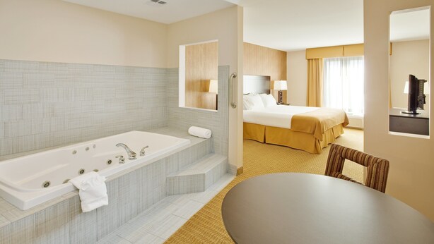 Ein modernes Hotelzimmer mit einer großen Badewanne, einem separaten Schlafbereich, einem Essbereich und einem Fernseher.