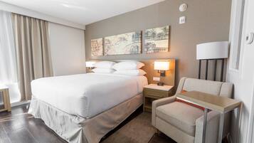 A hotel room with a large bed, bedside tables with lamps, a chair, and artwork on the wall.