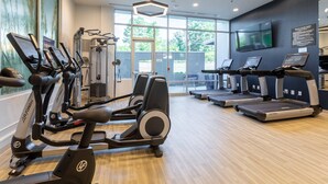 A modern gym with cardio machines, weight equipment, and a large window offering a view of the outdoors. - Delta Hotels by Marriott Raleigh-Durham at Research Triangle Park (Durham)