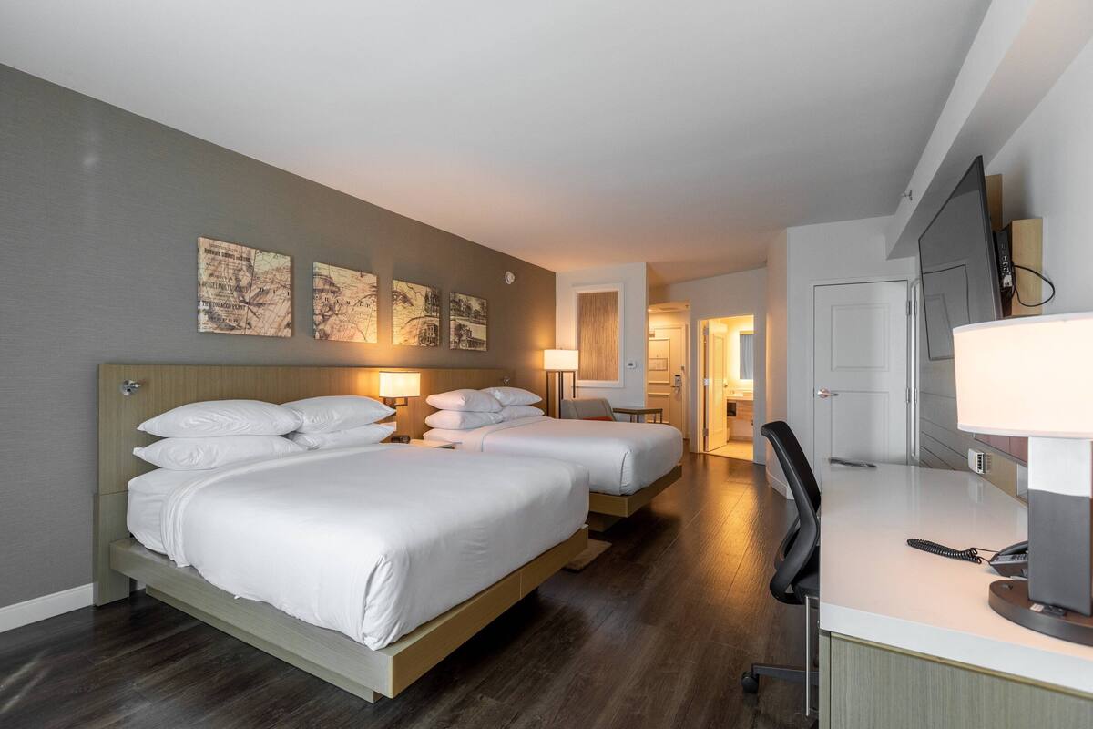 A hotel room with two beds, a desk, a chair, and a TV.