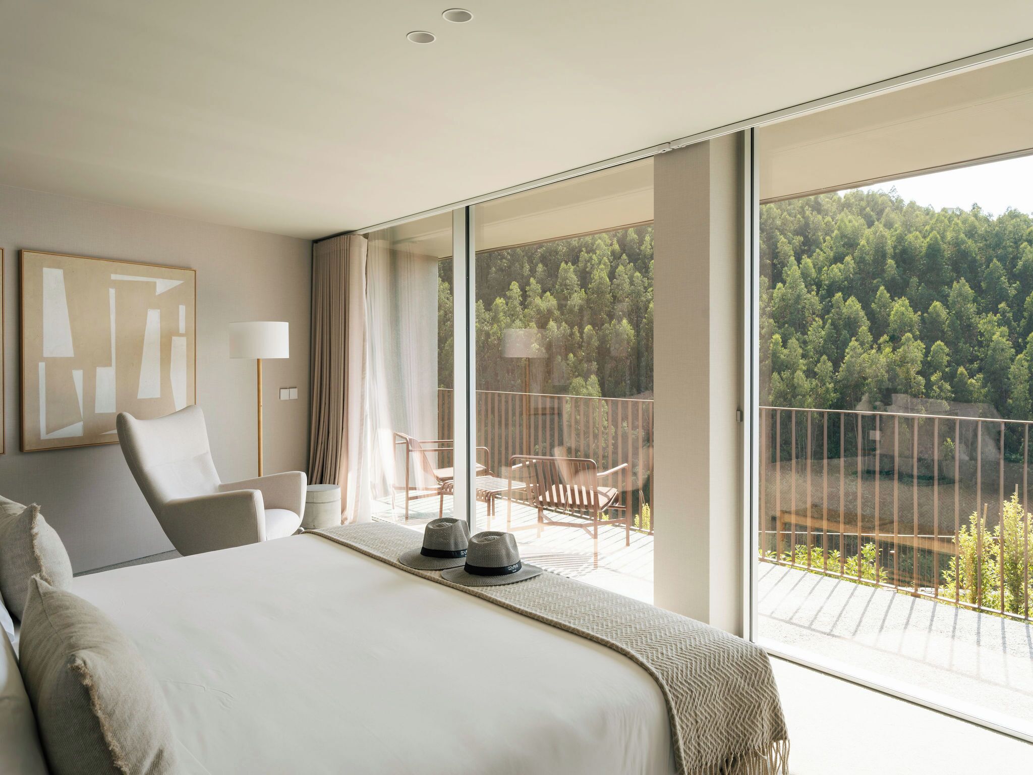 A hotel room with a large bed, a balcony with a view of a forest, and a modern design.