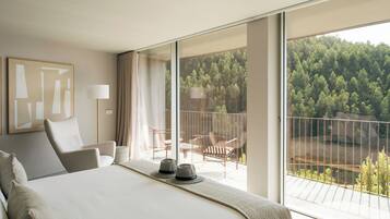 A hotel room with a large bed, a balcony with a view of a forest, and a modern design.