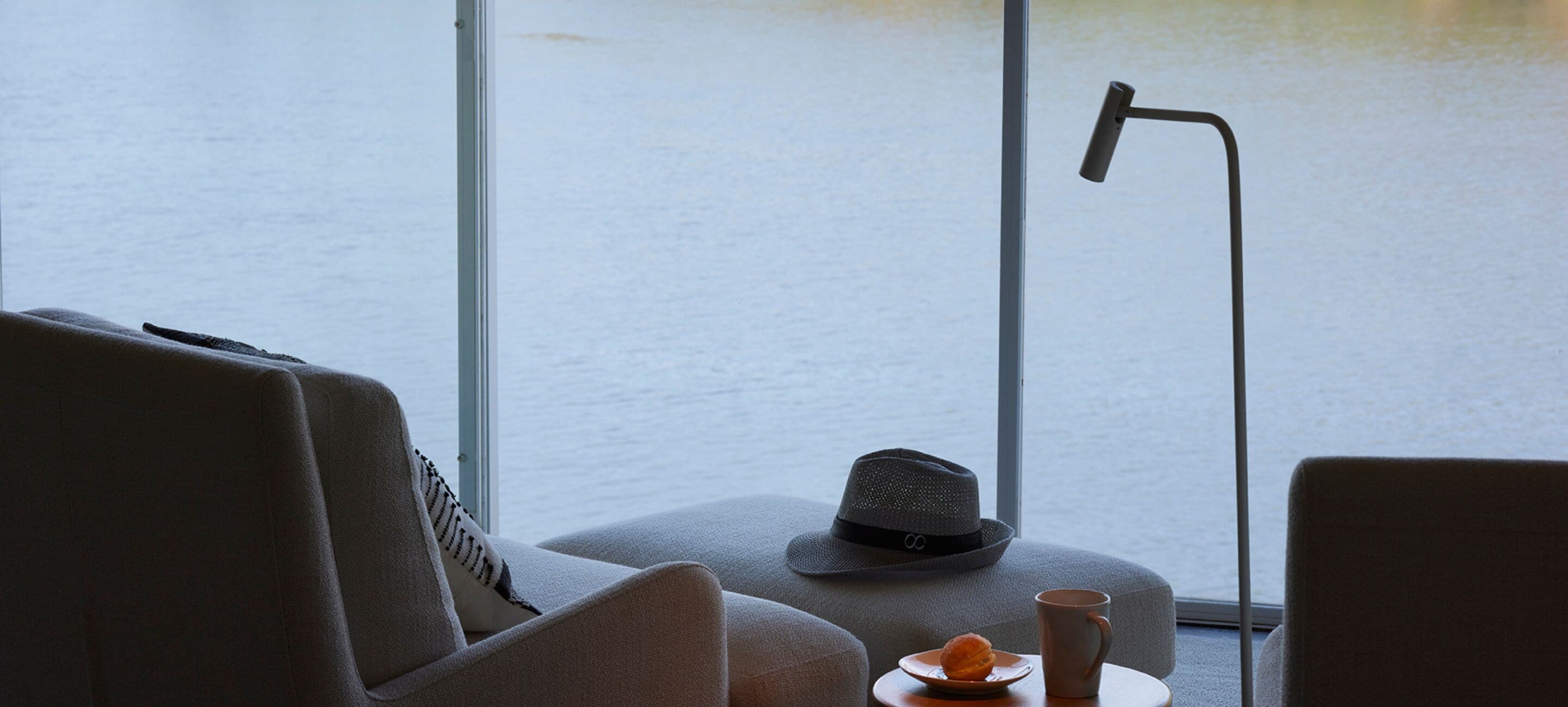 A room with a large window, a hat, a plate with a pastry, and a mug on a small table.