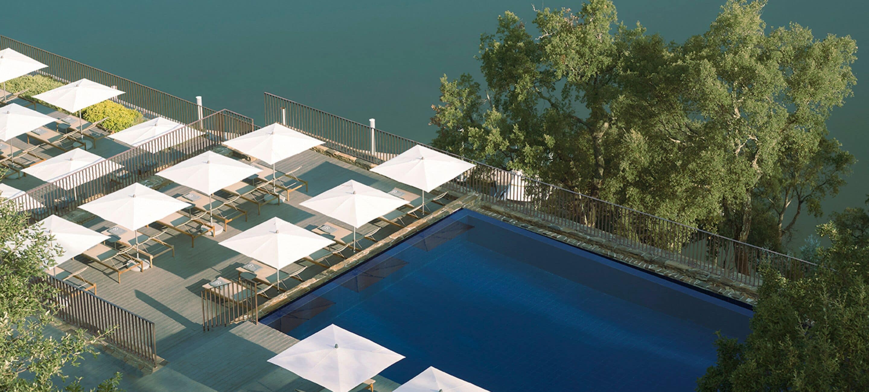 An aerial view of a swimming pool with sun loungers and umbrellas, surrounded by trees and a railing.