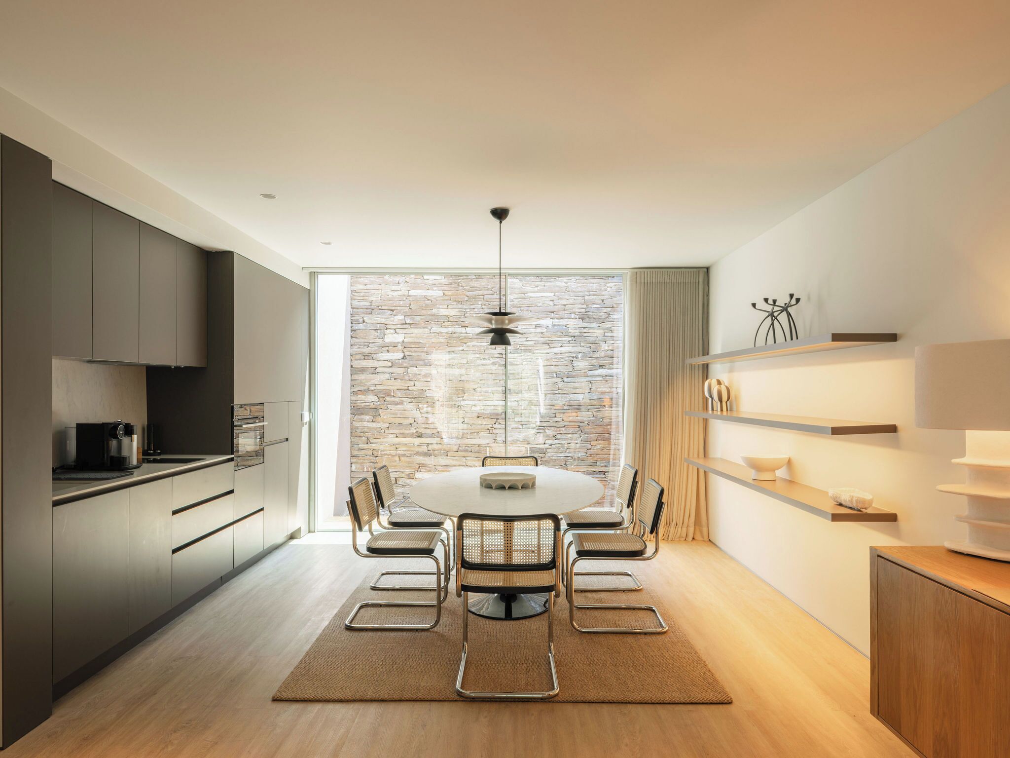 Une cuisine moderne avec un coin repas, comprenant un mur en pierre, une table ronde et des meubles contemporains.