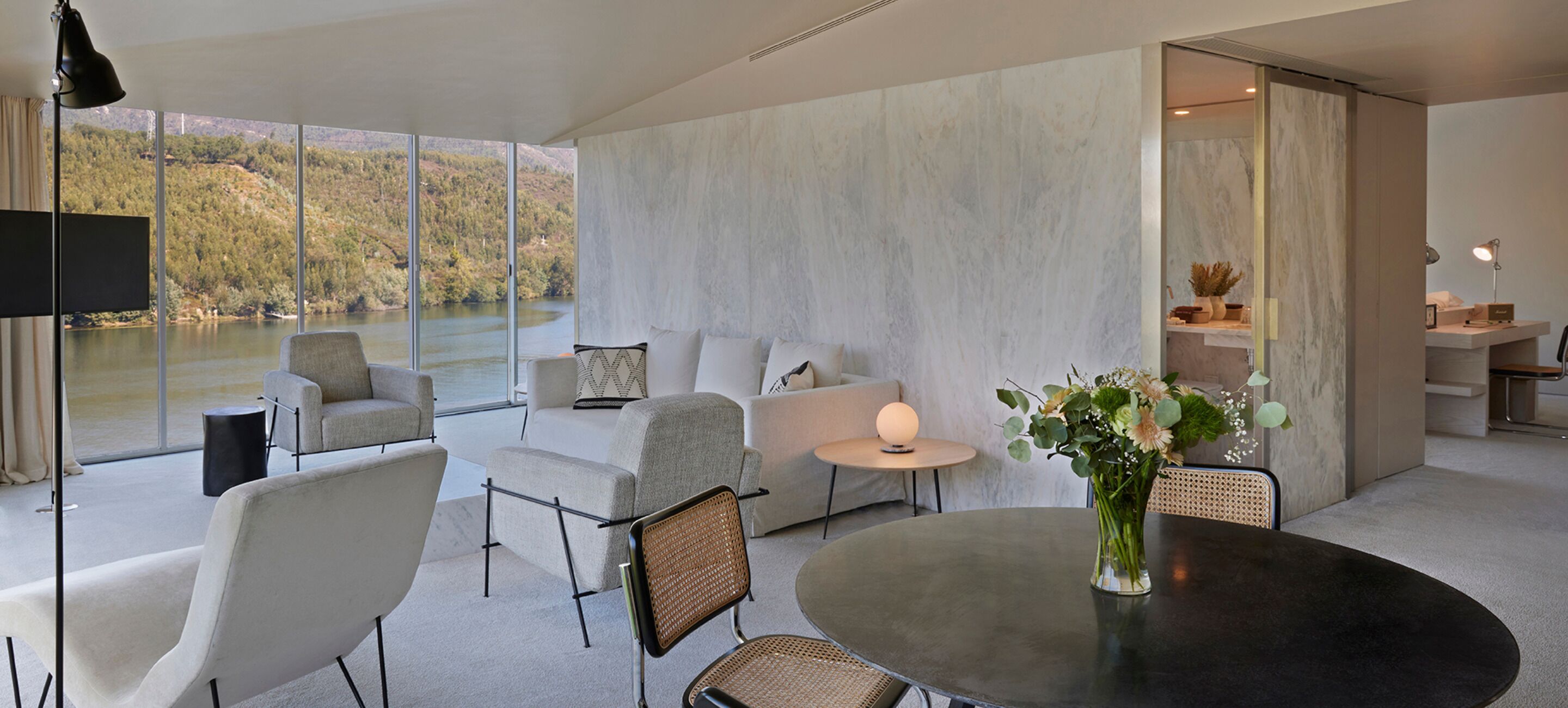 A modern living room with a large window overlooking a lake, a round dining table, and a seating area with sofas and chairs.