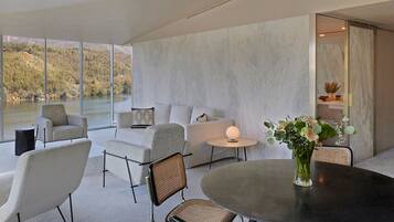 A modern living room with a large window overlooking a lake, a round dining table, and a seating area with sofas and chairs.
