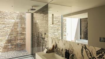 A modern bathroom with a large mirror, a dual sink, and a stone wall.