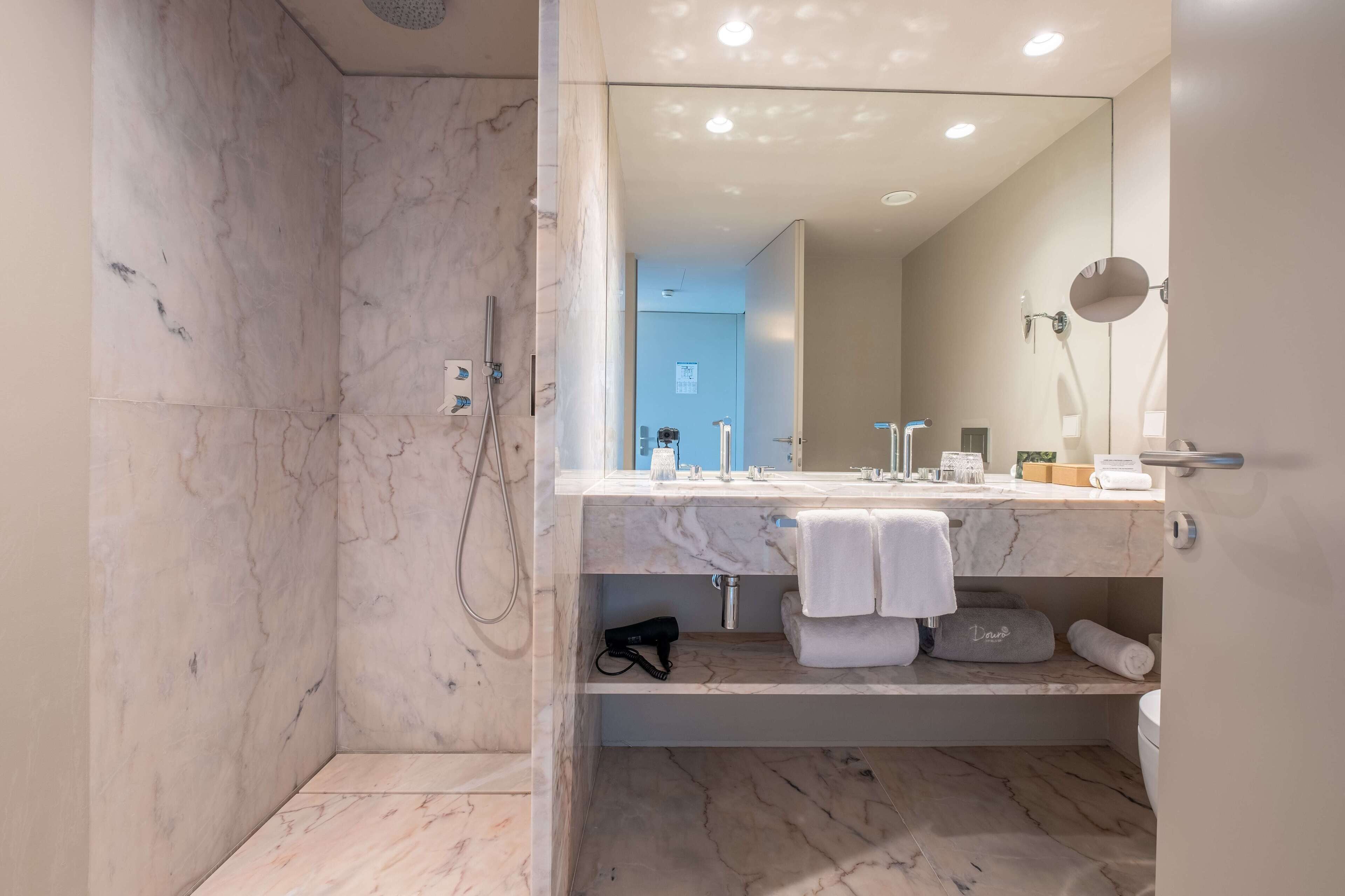 A modern bathroom with a marble shower, a large mirror, and a vanity with a towel rack.