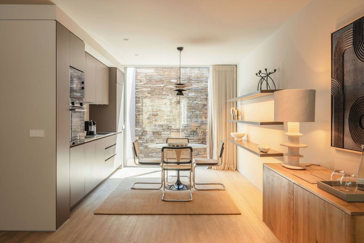 A modern kitchen with a stone wall, wooden cabinets, and a dining area with a table and chairs.
