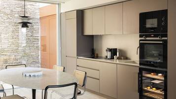 Een moderne keuken met een stenen muur, een eettafel met stoelen en inbouwapparatuur, waaronder een koffiezetapparaat en een oven.