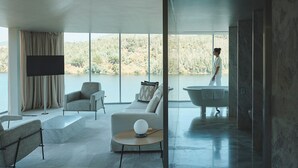 A modern living room with a large window, a flat-screen TV, a sofa, and a bathtub. - Octant Douro (Castelo de Paiva)