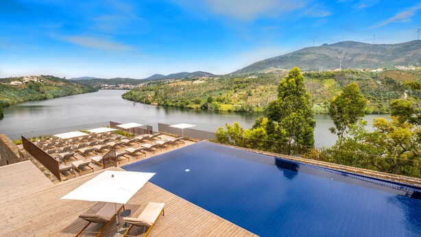 A pool with a view of a river and mountains, surrounded by lounge chairs and umbrellas. - Octant Douro (Castelo de Paiva)
