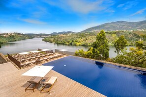 A pool with a view of a river and mountains, surrounded by lounge chairs and umbrellas. - Octant Douro (Castelo de Paiva)