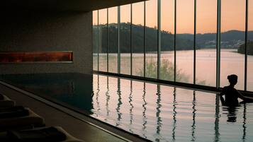 A pool area with a view of a lake and hills, a sauna, and a massage chair area.