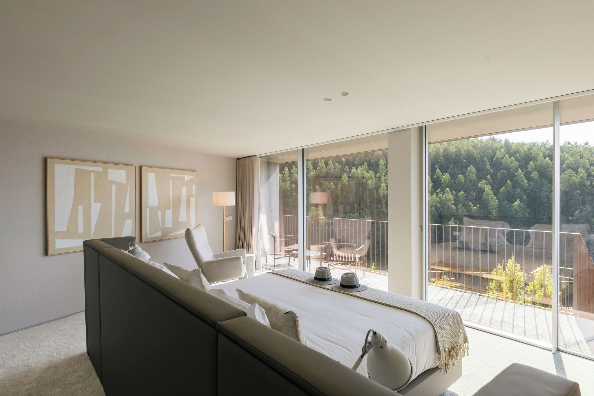 Quarto moderno com cama grande, duas mesinhas de cabeceira, uma cadeira e varanda com vista para árvores.
