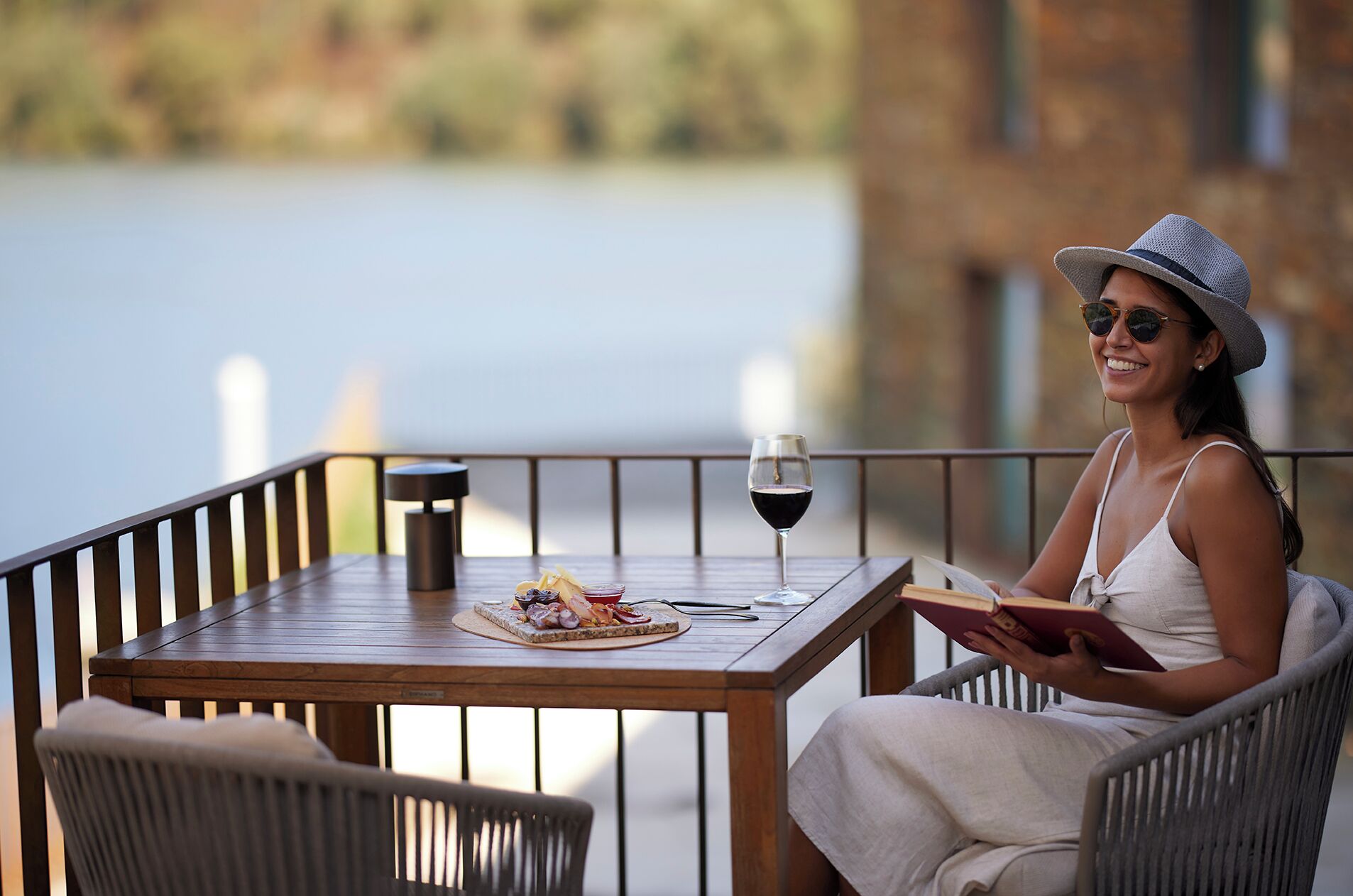 A person seated at a wooden table with a glass of red wine, a plate of food, and a book.