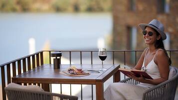 A person seated at a wooden table with a glass of red wine, a plate of food, and a book.