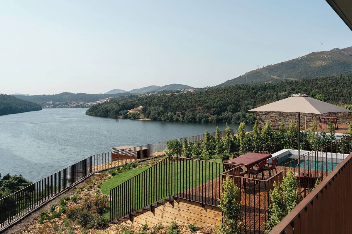 A deck with a pool, overlooking a river and hills.