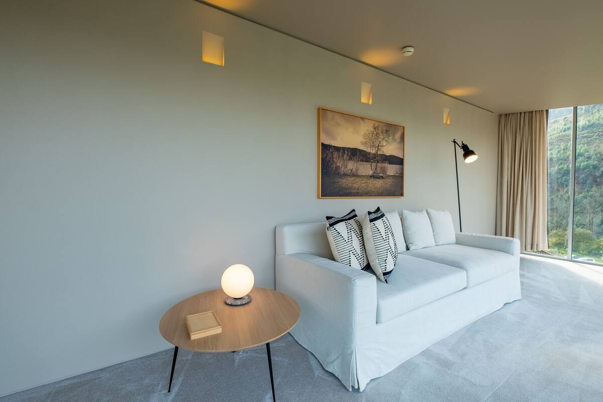 A modern living room with a white sofa, a round wooden side table, a floor lamp, and a painting on the wall.
