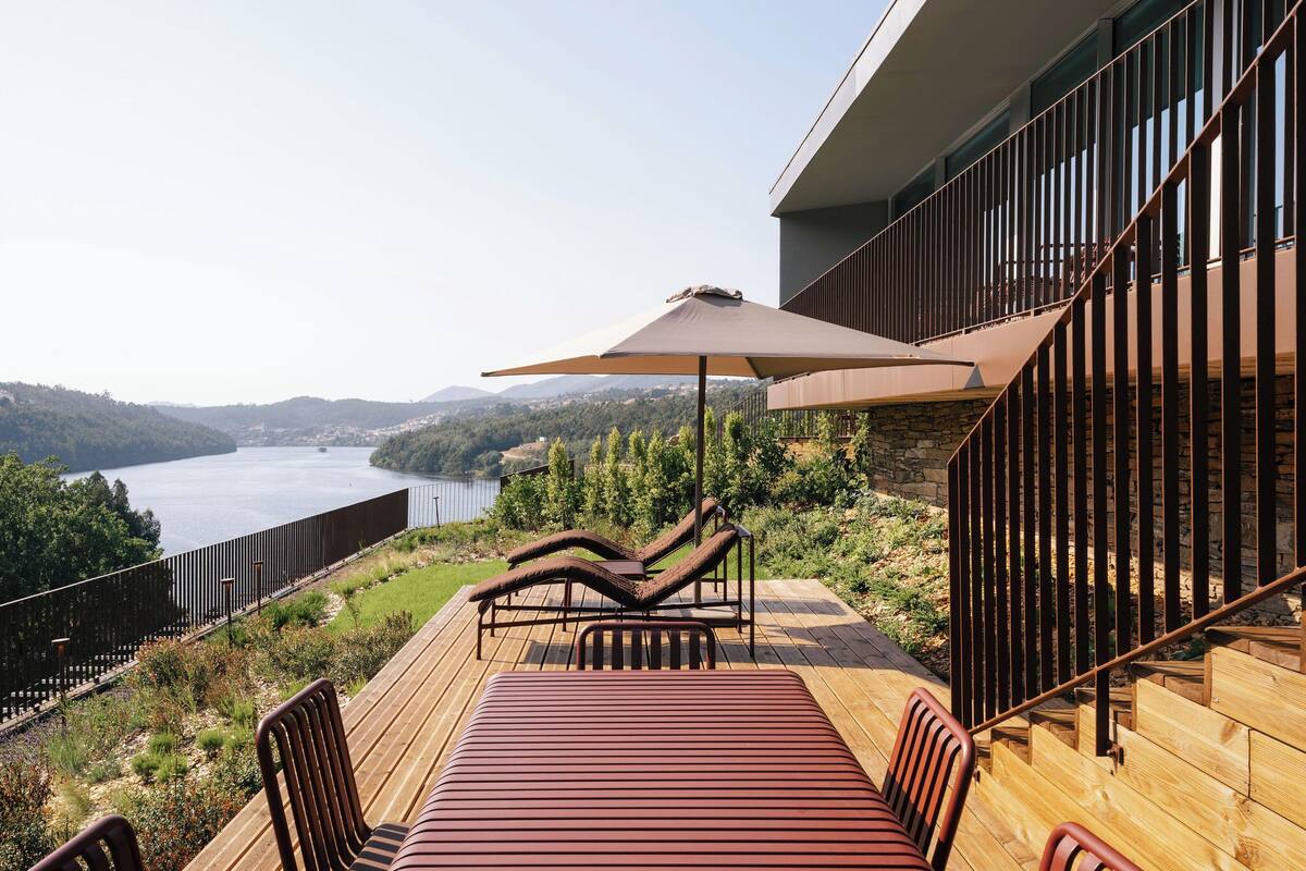 A deck with a table and chairs, overlooking a lake and hills.