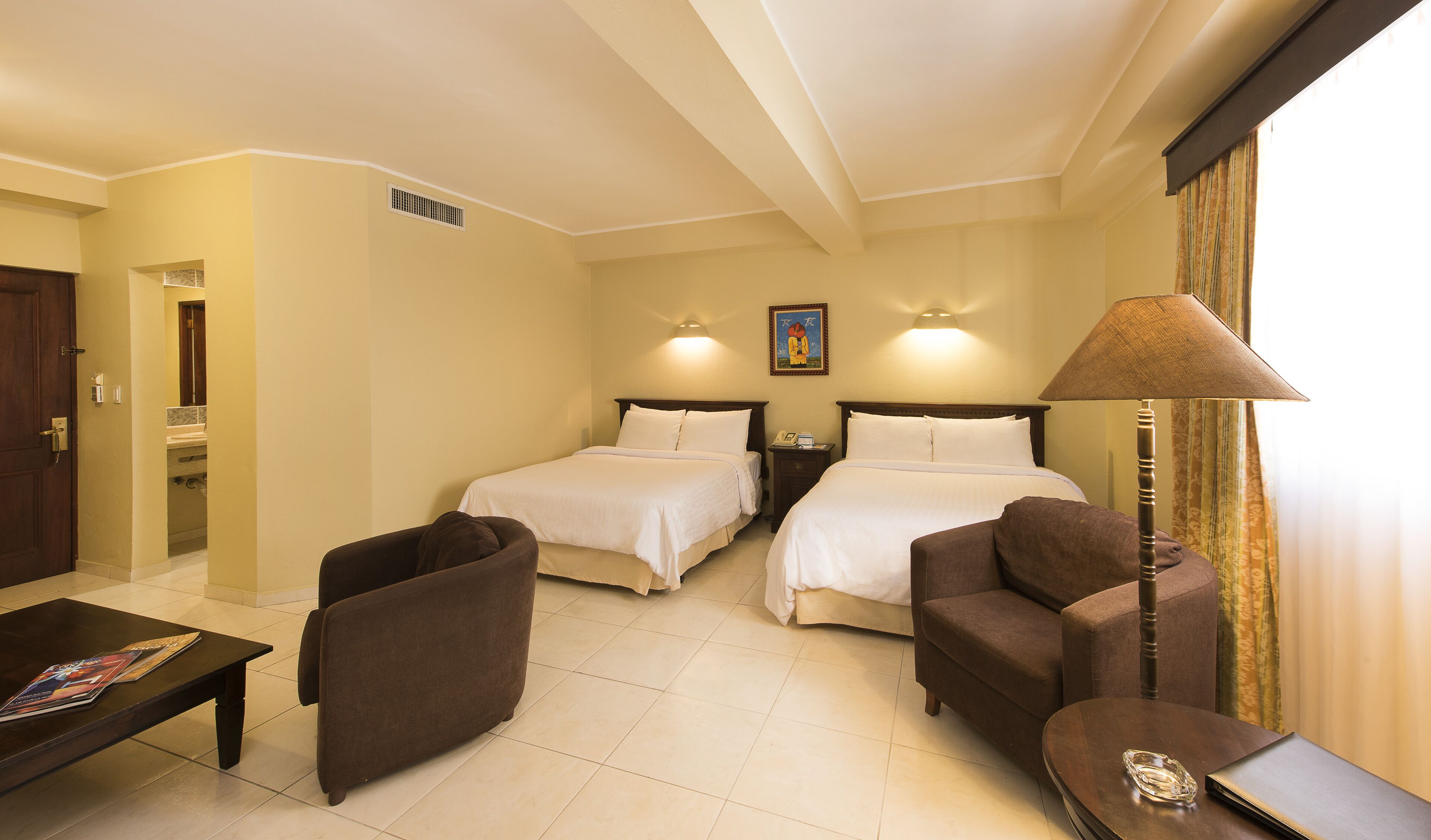 A hotel room with two beds, a sofa, a coffee table, and a lamp.