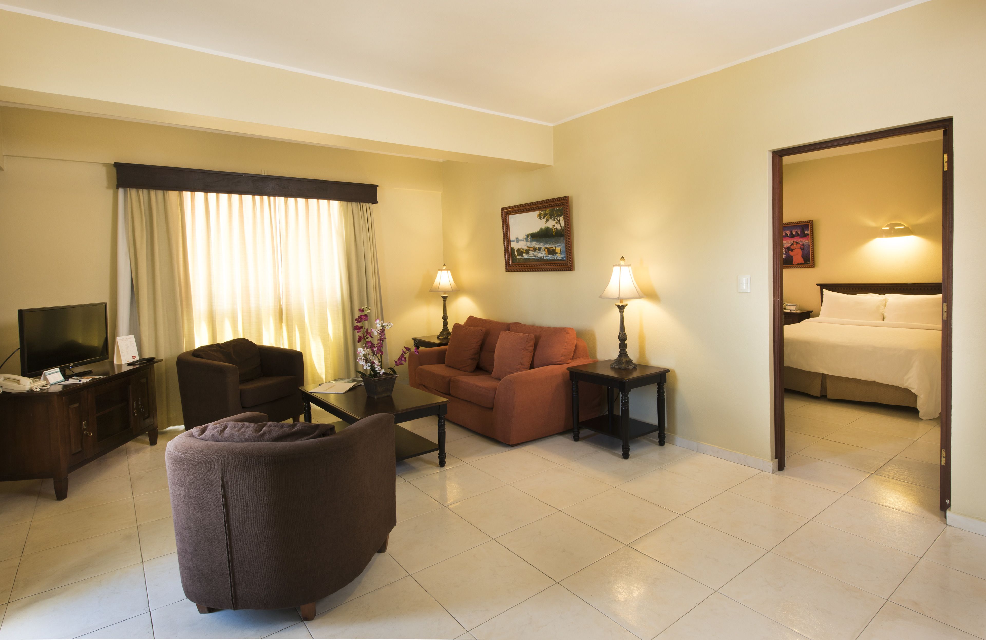 Quarto de hotel com área de estar, incluindo sofá, poltrona, mesa de centro e televisão.