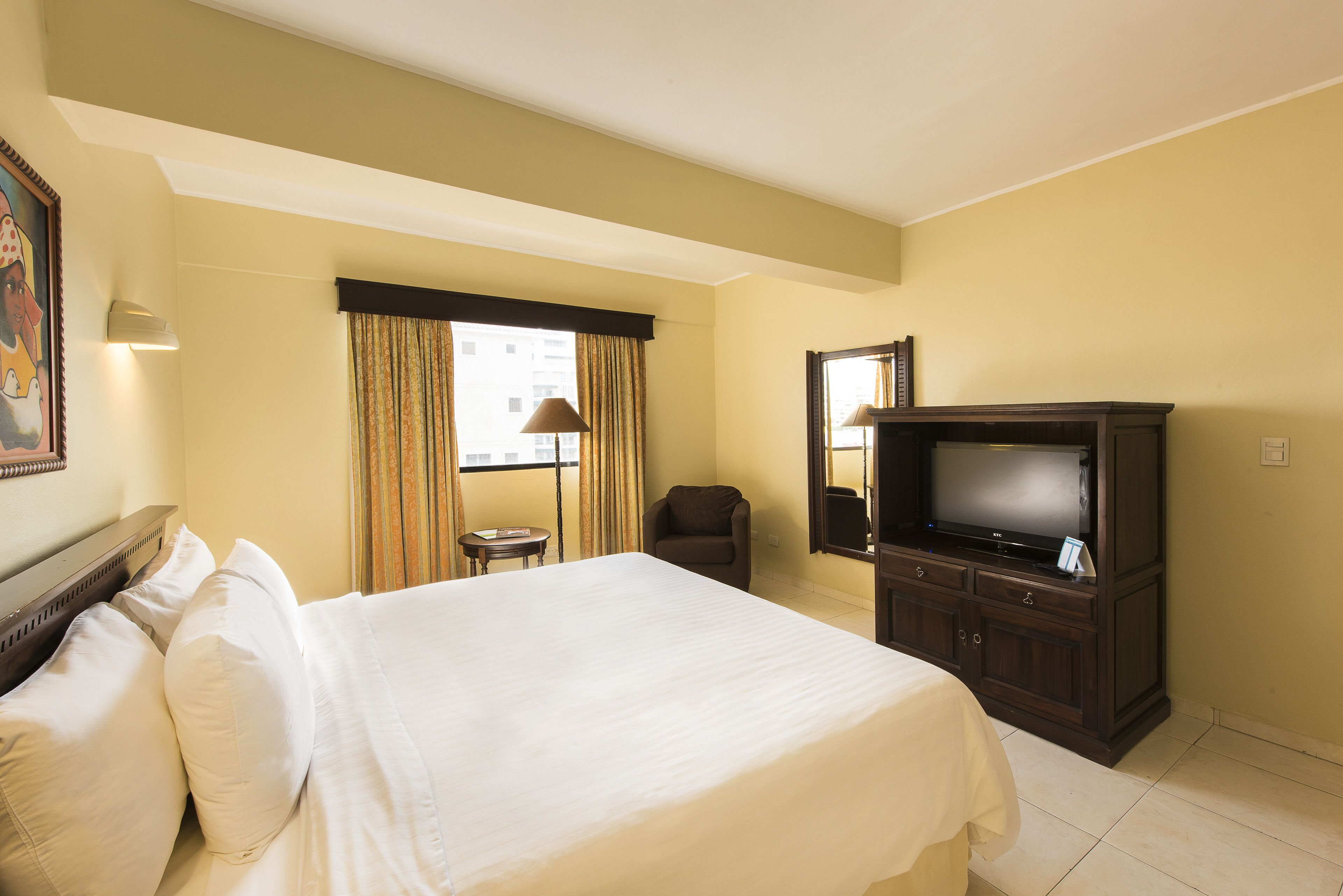 Una habitación de hotel con una cama grande, televisión, una mesita y una silla.