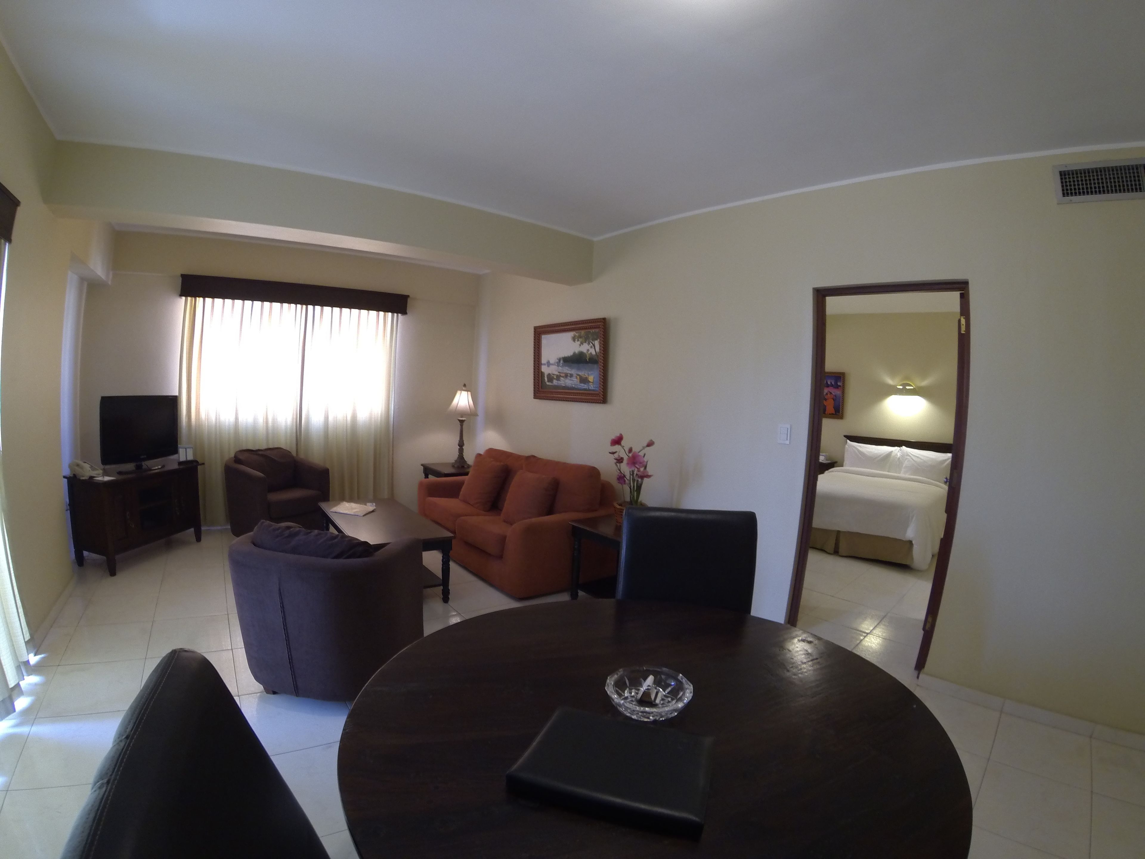 Quarto de hotel com sala de estar, incluindo TV, sofá, poltrona e mesa de jantar com cinzeiro de vidro.