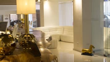 Uma sala de estar moderna com um sofá branco, uma divisória de vidro e um objeto decorativo dourado sobre uma mesa.