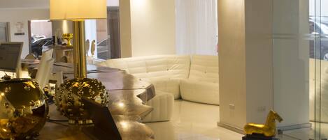 Una sala de estar moderna con un sofá blanco, un panel de vidrio y un adorno dorado sobre una mesa.